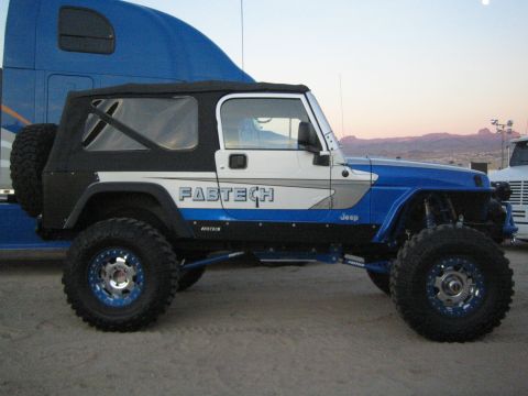 1990 Ford Bronco - Side profile of a blue and white lifted Jeep Wrangler with Fabtech decals and oversized off-road tires at dusk.