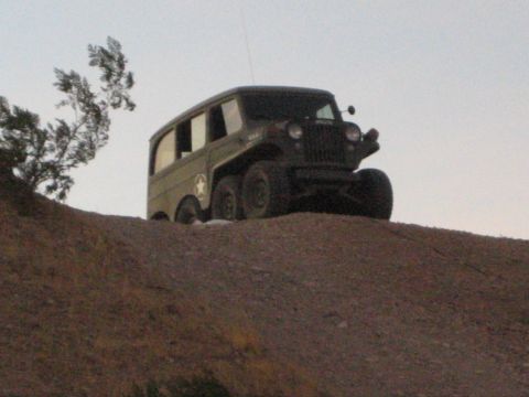 1990 Ford Bronco - olive-drab military-style six-wheel jeep with a white star marking, silhouetted on a dirt ridge against an evening sky.