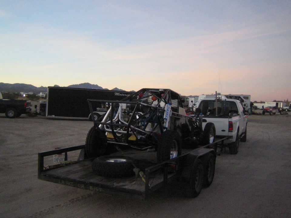 White pickup towing a trailer loaded with an off-road tube buggy at dusk