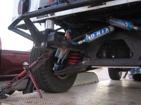 1990 Ford Bronco - Close-up of an off-road vehicle's front suspension featuring a King bypass coilover shock, red coil spring, and chained tie-down.