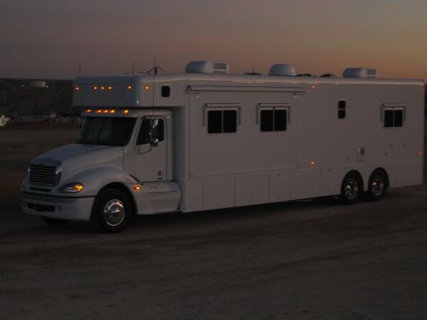 1990 Ford Bronco - white Freightliner-cab conversion motorhome with a large box body sits in a desert lot under a fading dusk sky.