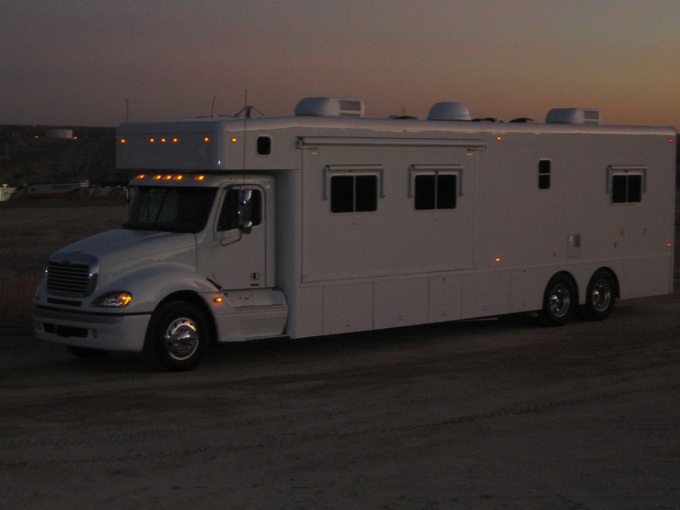 White Freightliner conversion motorhome with rear box body parked in desert at dusk