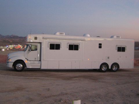1990 Ford Bronco - Side view of a white Freightliner-cab conversion motorhome parked on desert dirt at dusk with distant hills behind.