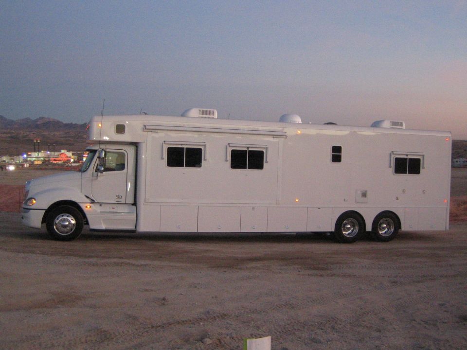 White Freightliner conversion motorhome side view parked in desert at dusk