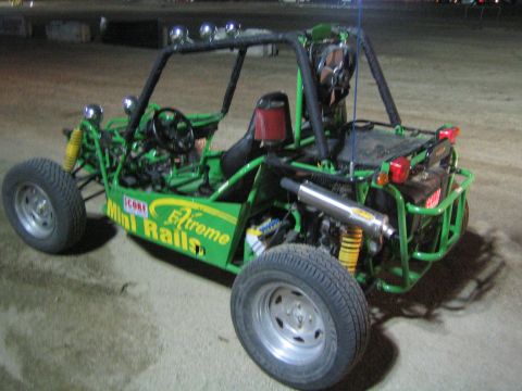 1990 Ford Bronco - green tube-frame sand rail buggy lettered "Extreme Mini Rails" sits on dirt at night, showing its roll cage, seats and rear engine.