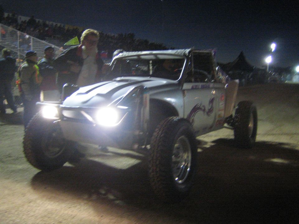 White off-road race truck with lights on driving past spectators at night