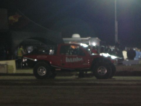 1990 Ford Bronco - red off-road truck lettered "banks" runs a dirt course at night in front of a lit grandstand crowd.
