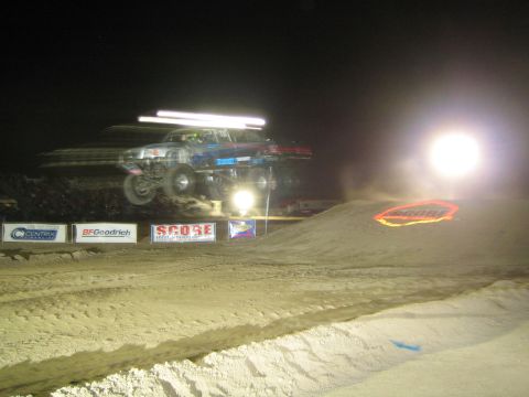 1990 Ford Bronco - off-road truck with a roof light bar leaps a dirt jump at night in front of SCORE and BFGoodrich banners.