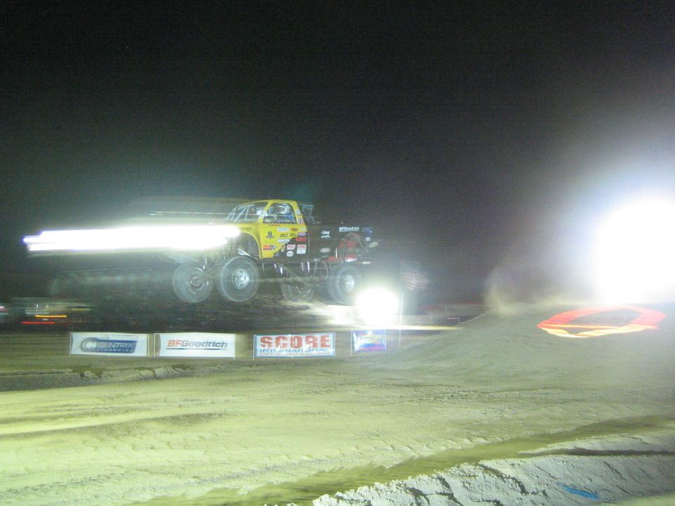Yellow off-road truck jumping at night with motion-blurred headlight streaks