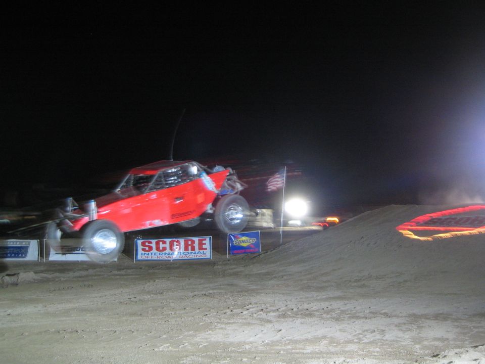 Red off-road race buggy airborne at night over a dirt jump