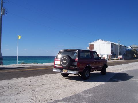 1995 Ford Bronco - A red Ford Bronco is parked by the beach on a sunny day with the ocean in the background.