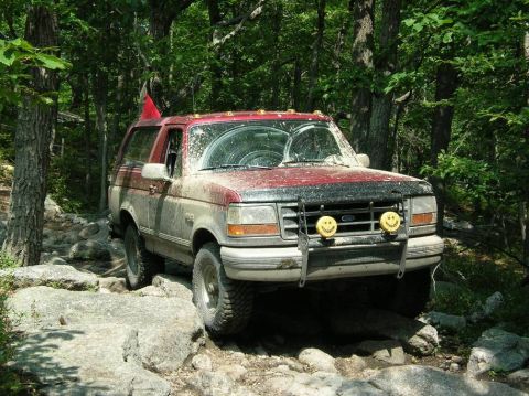 1995 Ford Bronco - A muddy Ford Bronco navigates a rocky path through a dense forest.