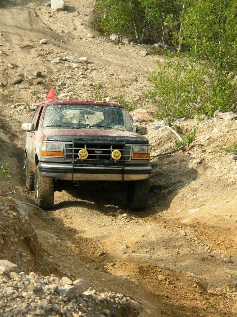 1995 Ford Bronco - A red Ford Bronco navigates a steep, rocky incline on a dirt trail.