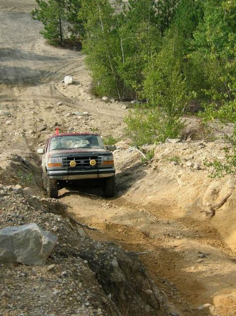 1995 Ford Bronco - A red Ford Bronco navigates a challenging dirt path, demonstrating its off-road capabilities.