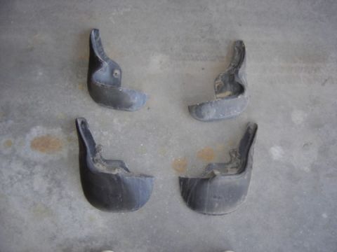 1999 Ford Taurus - Four used mud flaps are laid out on a gray concrete surface.