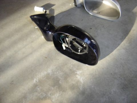 1999 Ford Taurus - A car side mirror assembly is shown disassembled on a concrete surface.