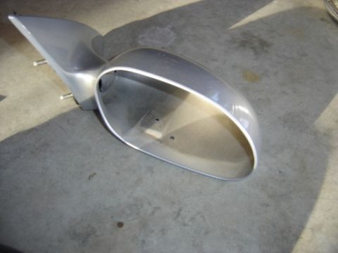 1999 Ford Taurus - A detached silver car side mirror housing rests on a concrete surface, casting a shadow.