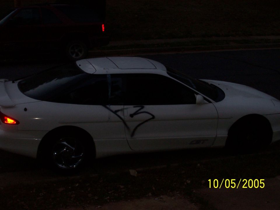 White coupe with graffiti on the side, seen from the side. The car has a sunroof and aftermarket wheels