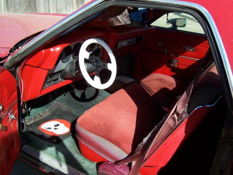 1979 Ford Ranchero - The interior of a red vehicle features a custom steering wheel and a unique floor mat with a ghost design.
