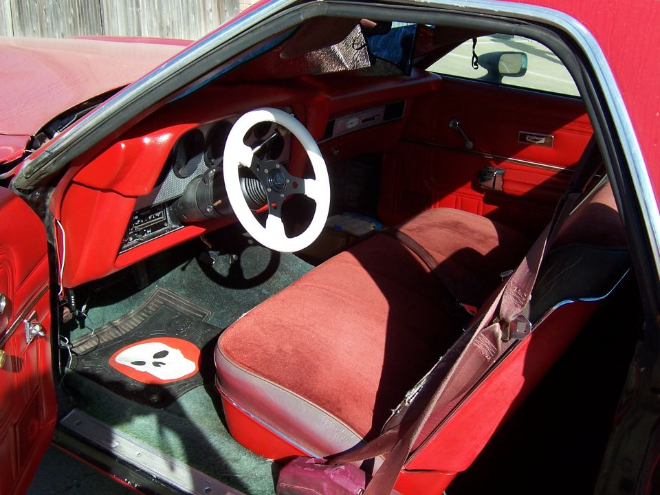 Red car interior with white steering wheel, red seats, and a ghost-shaped floor mat