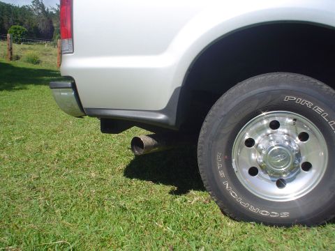 2005 Ford Excursion - Close-up of the rear wheel and exhaust of a silver truck parked on grass.