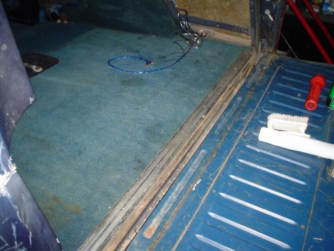 1984 Ford Bronco - Interior view of a vehicle showing blue carpet, exposed wiring, and a blue metal cargo floor with cleaning supplies.