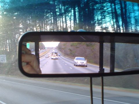1966 International School Bus - Traffic moves along a highway, seen through the reflection in a vehicle's rearview mirror.