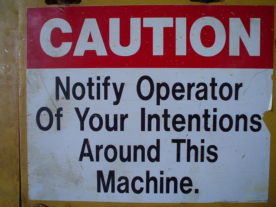Caution sign with text 'Notify Operator Of Your Intentions Around This Machine' on a yellow background