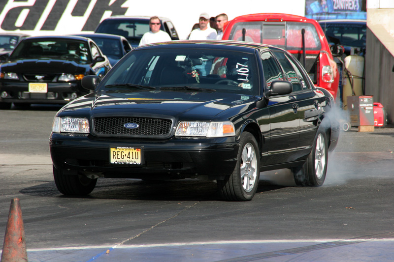Black 2004 Ford Crown Victoria on drag strip, front view, emitting smoke