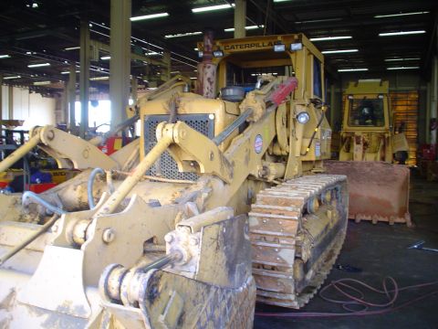 1966 International School Bus - A yellow Caterpillar bulldozer is parked inside a garage, with another similar vehicle in the background.