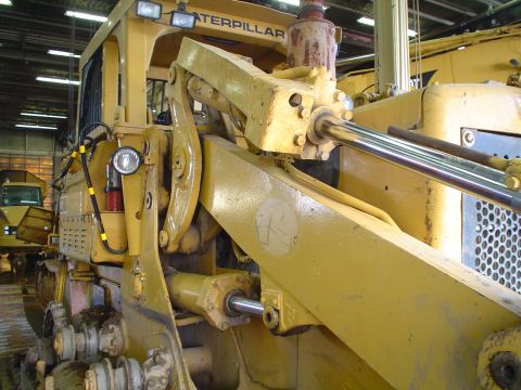 1966 International School Bus - Close-up view of a yellow bulldozer's hydraulic system and tracks, with another construction vehicle visible in the background.