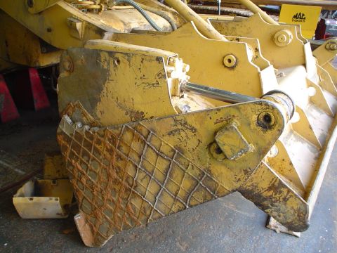 1966 International School Bus - Close-up of a weathered yellow heavy machinery component, showing hydraulic cylinder and diamond plate texture.