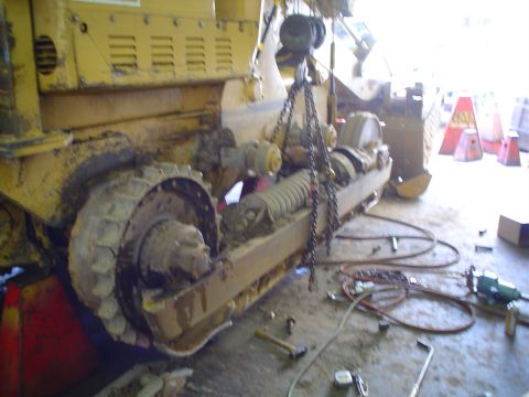 1966 International School Bus - Heavy machinery with tracks and chains is undergoing repairs in a workshop setting.