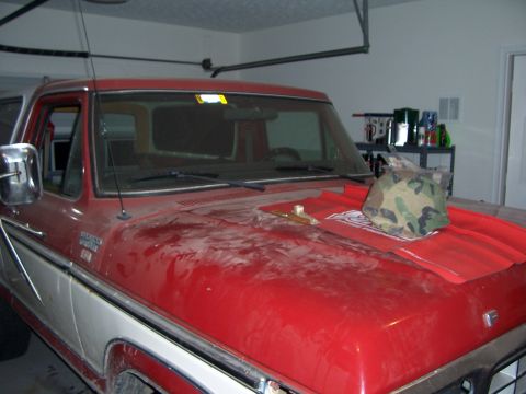 1978 Ford Bronco - A red and white 1978 Ford Bronco is parked in a garage with a camouflage helmet resting on its hood.
