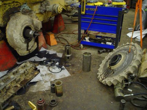 1966 International School Bus - Shop floor littered with greasy parts from a disassembled piece of heavy equipment, with a blue tool chest nearby.