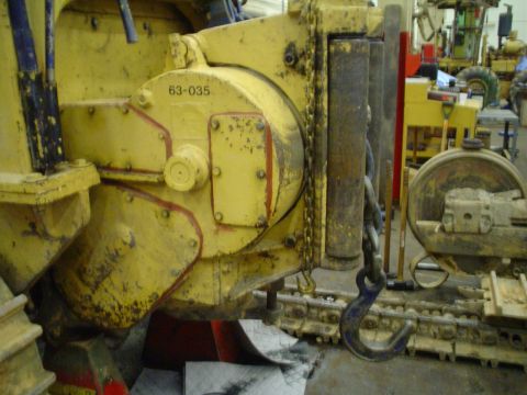 1966 International School Bus - Close-up of yellow heavy machinery part with visible chain and hook, with other equipment in the background.