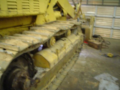 1966 International School Bus - Close-up of the tracks and suspension system of a large yellow crawler tractor inside a garage.