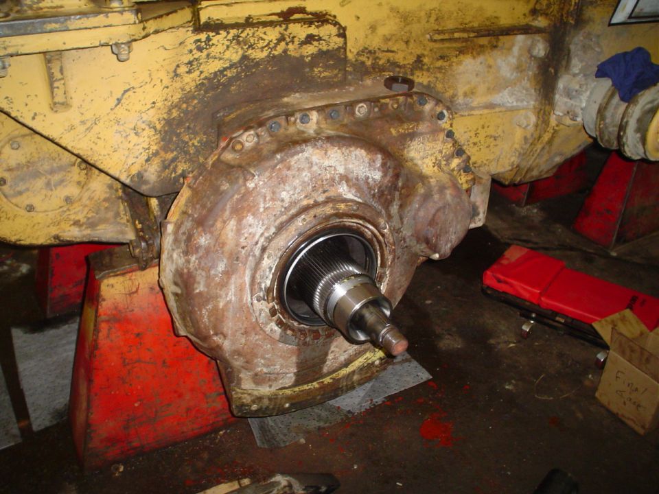 Yellow heavy machinery axle housing with splined shaft, supported by red jack stands