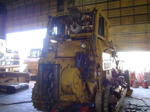 1966 International School Bus - A yellow Caterpillar tractor is parked inside a garage, with another piece of heavy machinery visible in the background.