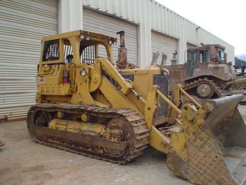 1966 International School Bus - A Caterpillar bulldozer is parked in front of a building, with another bulldozer visible behind it.