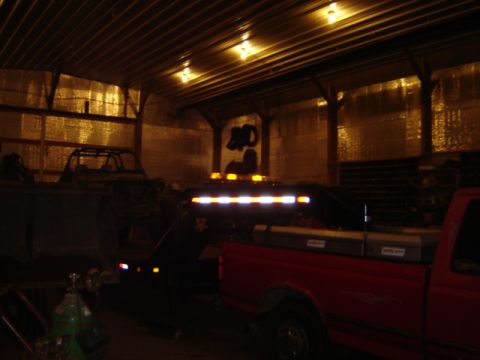1992 Ford Bronco - A red pickup truck is parked inside a barn, hitched to a trailer with multiple amber lights.