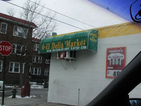 1992 Ford Taurus - A storefront awning displays "6-11 Delis & Market" along with a phone number and a list of items sold.