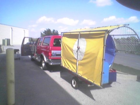 1994 Ford C-150 (Centurion Conversions) - A red SUV is parked with its door open, hitched to a trailer covered in yellow fabric.