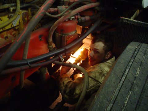1966 International School Bus - A mechanic is seen working on the engine of a vehicle, illuminated by a flashlight. A tire is visible in the foreground.