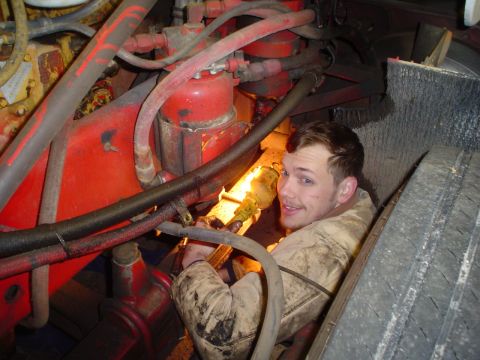 1966 International School Bus - A mechanic is seen working deep within the engine bay of a large vehicle, illuminated by a flashlight.