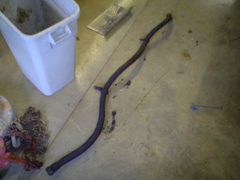 1966 International School Bus - A dark, curved hose or pipe is shown on a concrete floor, beside a white plastic bin and a pile of chains.