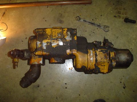 1966 International School Bus - A greasy hydraulic pump sits on a workshop floor next to a wrench and other parts.