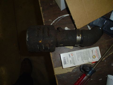1966 International School Bus - A dirty exhaust pipe assembly, possibly from a diesel engine, rests on a cluttered wooden surface.
