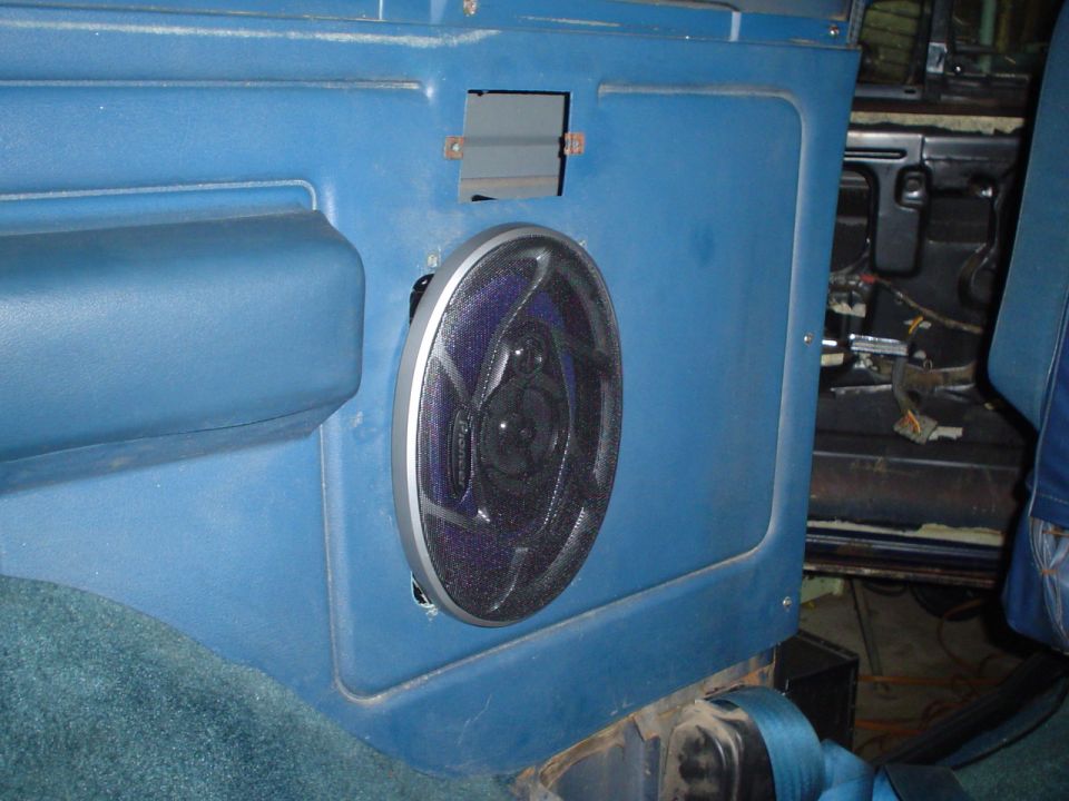 Blue interior door panel with a round speaker installed. Wires are visible behind the panel