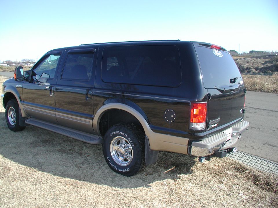 Black and tan Ford Excursion SUV rear three-quarter view on dirt with chrome wheels